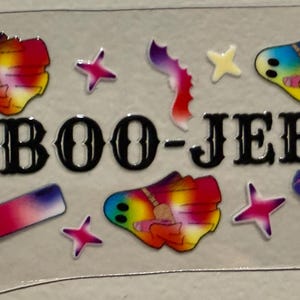 Puede incluir: Una lámina de pegatinas transparente con diseños coloridos y el texto "BOO-JEE". La lámina incluye formas abstractas, estrellas y diseños rectangulares con degradados rojos, rosas, azules y amarillos. La lámina es sostenida por una mano.