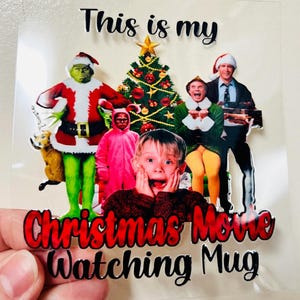 May include: A clear sticker with the text "This is my Christmas Movie Watching Mug." The sticker features images of characters from popular Christmas movies, including the Grinch, Kevin McCallister, and Buddy the Elf, with a decorated Christmas tree.