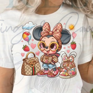 May include: White t-shirt featuring a cartoon Minnie Mouse character wearing sunglasses, a bow, and a jacket. The design includes a handbag, shoes, hearts, a balloon, a cloud, a sun, and strawberries. The character is wearing denim shorts and pink shoes.