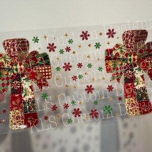 Peut inclure: Deux appliqués en forme de croix sur le thème de Noël, avec un motif patchwork rouge, vert et or. Les appliqués présentent un nœud en haut et sont décorés de flocons de neige et d'étoiles. Le texte "KLS Custom Designs" est visible.