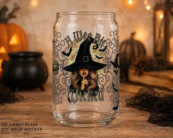 May include: A clear glass can-shaped tumbler featuring a graphic of a witch wearing a black hat with a finger to her lips. The design includes a full moon, black bats, swirling filigree patterns, and the text A Wee Bit Wicked in black font.