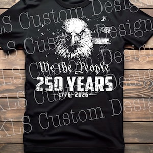 Op de afbeelding: Zwart T-shirt met een witte afbeelding van een adelaarskop en de tekst "We the People 250 YEARS 1776-2026". Het ontwerp heeft een distressed effect. Het T-shirt heeft een ronde hals en korte mouwen.