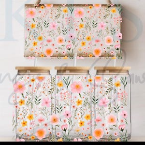 Puede incluir: Un letrero de madera y tres frascos de vidrio con diseños florales. El letrero y los frascos presentan un patrón repetido de flores rosas, amarillas y naranjas con hojas verdes. Los frascos tienen tapas de madera.