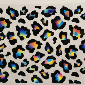 Puede incluir: Una lámina de vinilo transparente con un patrón de estampado de leopardo iridiscente arcoíris. La impresión es en blanco y negro con un brillo arcoíris.