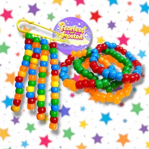 May include: A selection of vibrant beaded jewellery. The image shows a yellow safety pin adorned with strands of red, orange, yellow, green, and blue beads. Several beaded bracelets in various colours are also visible, alongside a circular badge reading "fearless and frosted."
