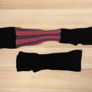 A close up shot of a pair of asymmetrical black gloves with purple and magenta striped detail