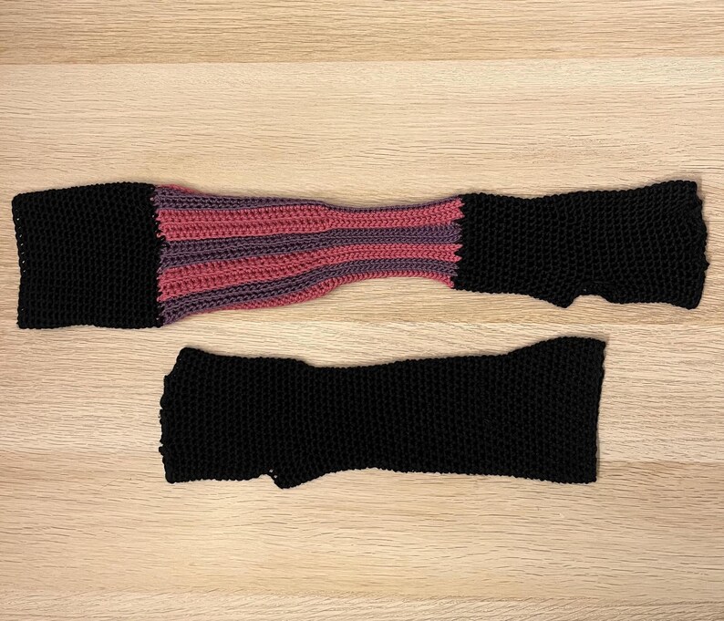 A close up shot of a pair of asymmetrical black gloves with purple and magenta striped detail