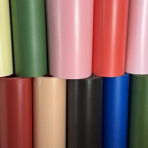 May include: A collection of rolled-up vinyl sheets in various colors, including yellow, green, pink, red, black, and blue. The rolls are stacked, showcasing the different hues and textures of the material.