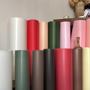 May include: A collection of cylindrical paper rolls in various colors, including white, red, pink, green, and brown. The rolls are arranged in a vertical display, showcasing their different hues and textures. Some rolls are standing upright, while others are partially visible.