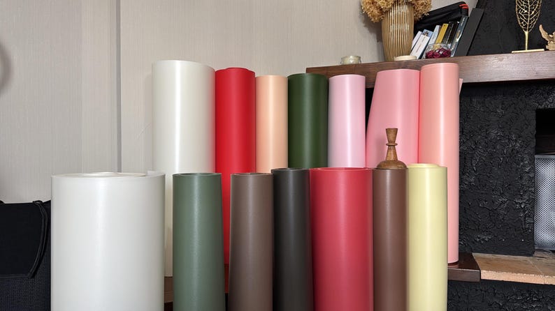 May include: A collection of cylindrical paper rolls in various colors, including white, red, pink, green, and brown. The rolls are arranged in a vertical display, showcasing their different hues and textures. Some rolls are standing upright, while others are partially visible.