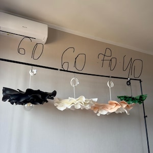 May include: Three decorative pendant lights with ruffled shades in black, cream, and peach colors hang from a black metal bar. The text "60 60 to 40" is written above the lights.