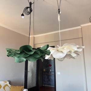May include: Two modern pendant lights with a floral design. One is green, the other is white. Both are suspended from the ceiling by black cords. The lights are in a living room setting.