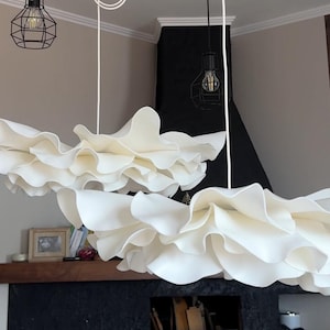 May include: Two white, cloud-like pendant lights with ruffled edges hang from the ceiling. The lights are suspended by white cords. Two black metal cage-style light fixtures with exposed bulbs are also visible.
