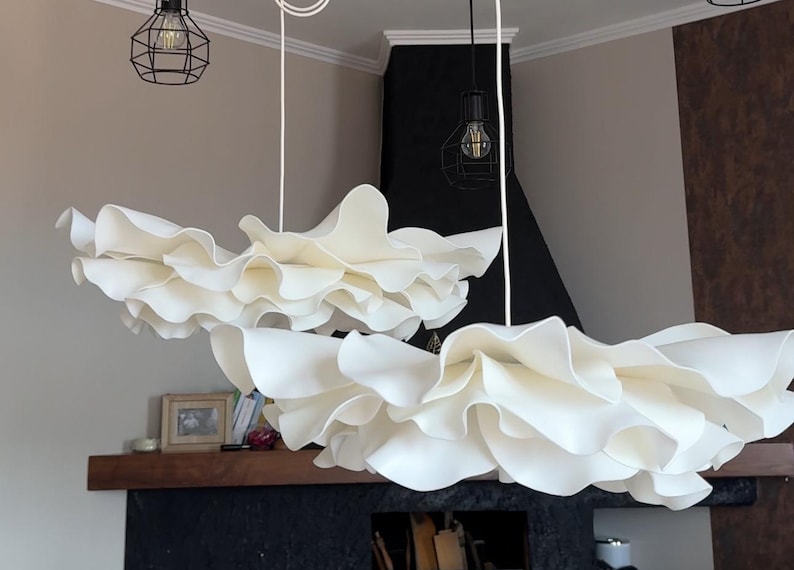May include: Two white, cloud-like pendant lights with ruffled edges hang from the ceiling. The lights are suspended by white cords. Two black metal cage-style light fixtures with exposed bulbs are also visible.