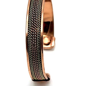 May include: Copper cuff bracelet with a woven design in shades of gold, silver, and copper. The bracelet has a magnetic clasp. This piece of jewelry is a stylish accessory.