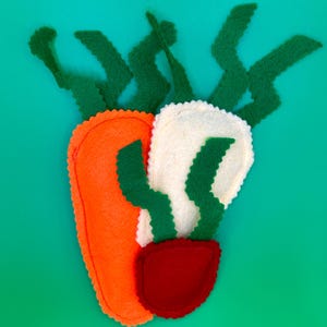 May include: A felt carrot and radish set with green tops and a red base, set against a teal background. The carrot is orange, and the radish is white. The edges are stitched with a contrasting thread.
