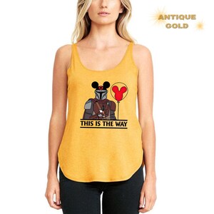 May include: A yellow tank top with a black and brown illustration of a character wearing a helmet and holding a red balloon with Mickey Mouse ears. The text "This is the way" is printed below the illustration.