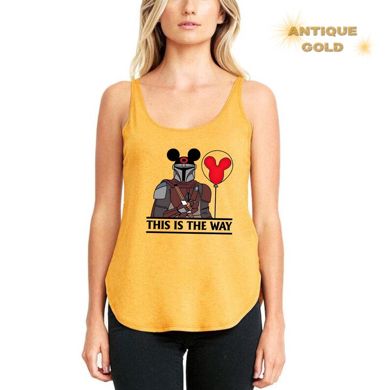 May include: A yellow tank top with a black and brown illustration of a character wearing a helmet and holding a red balloon with Mickey Mouse ears. The text "This is the way" is printed below the illustration.