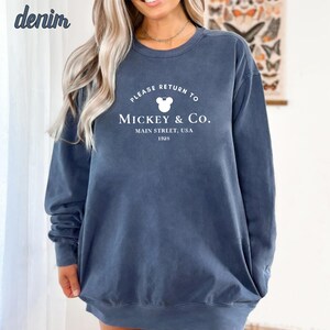 May include: A dark blue sweatshirt with a white graphic that says "Please Return To Mickey & Co. Main Street, USA 1925". The graphic also includes a white Mickey Mouse head.