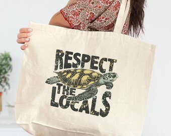 May include: Cream-colored tote bag featuring a sea turtle illustration and the text "RESPECT THE LOCALS" in distressed black lettering. The bag has a rectangular shape with a wide opening and long straps for carrying over the shoulder.