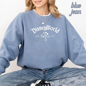 Puede incluir: Una sudadera azul claro con un gr&aacute;fico blanco de Mickey Mouse y el texto "Disneyworld Est. 1971".