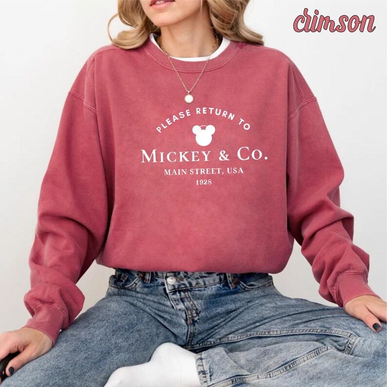 May include: A crimson sweatshirt with a white graphic that says "Please Return To Mickey & Co. Main Street, USA 1928" with a white Mickey Mouse head silhouette.