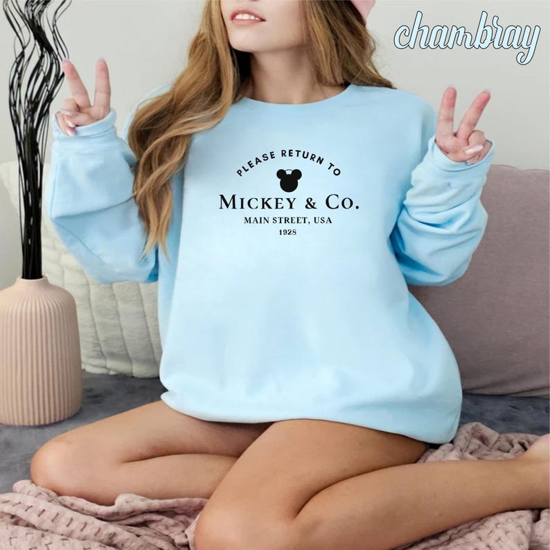 May include: Light blue sweatshirt with a black Mickey Mouse head and the text "Please return to Mickey & Co. Main Street, USA 1925"