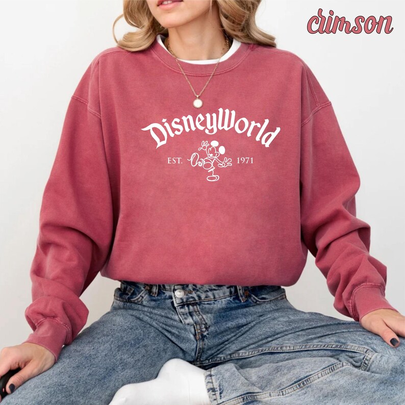 Puede incluir: Una sudadera de color rojo carmes&iacute; con un gr&aacute;fico blanco de Mickey Mouse y el texto "Disneyworld Est. 1971".