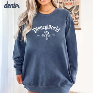Puede incluir: Una sudadera de manga larga azul oscuro con el texto "Disneyworld Est. 1971" y un contorno blanco de Mickey Mouse.