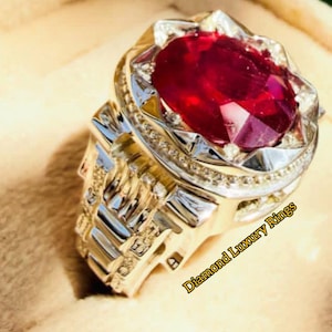 Pode incluir: Um anel ornamentado com uma vibrante pedra vermelha. A banda prateada apresenta detalhes intrincados e pequenas pedras de acento. O texto "Diamond Luxury Rings" é visível.