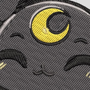 Puede incluir: Parche bordado con la cara de un gato de dibujos animados sonriente con un ojo de media luna. El gato es gris con detalles negros y una luna amarilla. El parche tiene un aspecto texturizado.