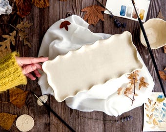 May include: A rectangular, off-white ceramic serving platter with a wavy edge. The platter is displayed on a white cloth, surrounded by fall leaves, paintbrushes, and watercolor art supplies. The overall theme is a rustic, artistic aesthetic.