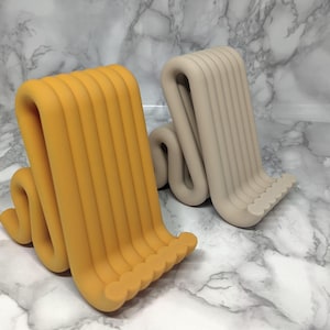 May include: Two abstract sculptures with a wavy design. One is mustard yellow, the other beige. Each has vertical, rounded ridges that curve and bend. The bases feature a row of small, rounded bumps. The sculptures are decorative.