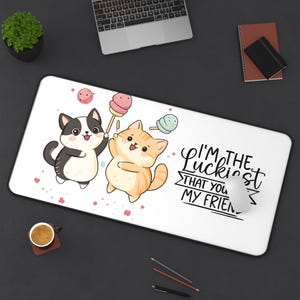 Può includere: Tappetino per mouse rettangolare bianco con due gatti dei cartoni animati che tengono lecca lecca. Un gatto è bianco e nero, l'altro è arancione e bianco. Il testo recita "I'M THE Luckiest THAT YOU MY FRIEN.". Ci sono spruzzi rosa e blu sparsi.