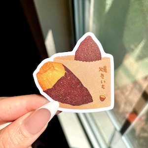 May include: A sticker featuring a stylized illustration of a baked sweet potato. The sticker has a brown paper bag design with a sweet potato peeking out. The Japanese text "焼きいも" is printed on the bag.