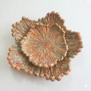 May include: A collection of handmade ceramic plates with a distinctive, textured design. The plates display a warm, earthy colour scheme of brown and orange, with hints of turquoise. Each plate has a scalloped edge.