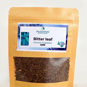 Puede incluir: Una bolsa de papel marrón con una ventana transparente, llena de hojas secas. La etiqueta de la bolsa dice "Bitter leaf (Vernonia amygdalina) Leaves" con una imagen de hojas turquesas y la marca "PleazantField".