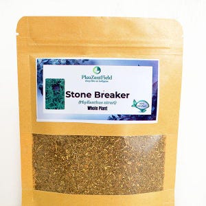 Op de afbeelding: Een bruine papieren zak met een transparant venster met gedroogde kruiden. Het etiket leest "Stone Breaker (Phyllanthus niruri) Whole Plant" en toont het "100% Organic" logo. De merknaam "PleazantField" is ook zichtbaar.