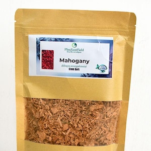 Può includere: Un sacchetto di carta marrone pieno di corteccia di fusto di mogano. La borsa ha un'etichetta bianca con il testo "Mahogany (Khaya senegalensis) Stem Bark" e un quadrato rosso. La borsa è sigillata con una chiusura a zip.