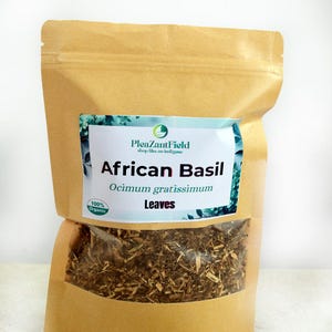 May include: A brown paper bag filled with dried African Basil leaves. The bag has a label with the text "PleazantField" and "African Basil Ocimum gratissimum Leaves". A smaller label reads "100% Organic".