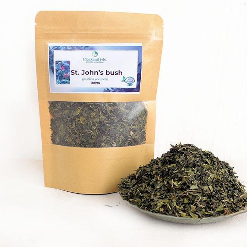 May include: A brown paper bag with a clear window, filled with dried green leaves. A small pile of the same leaves sits on a small, gray dish. The bag has a label that reads "St. John's bush (Justicia secunda) Leaves."