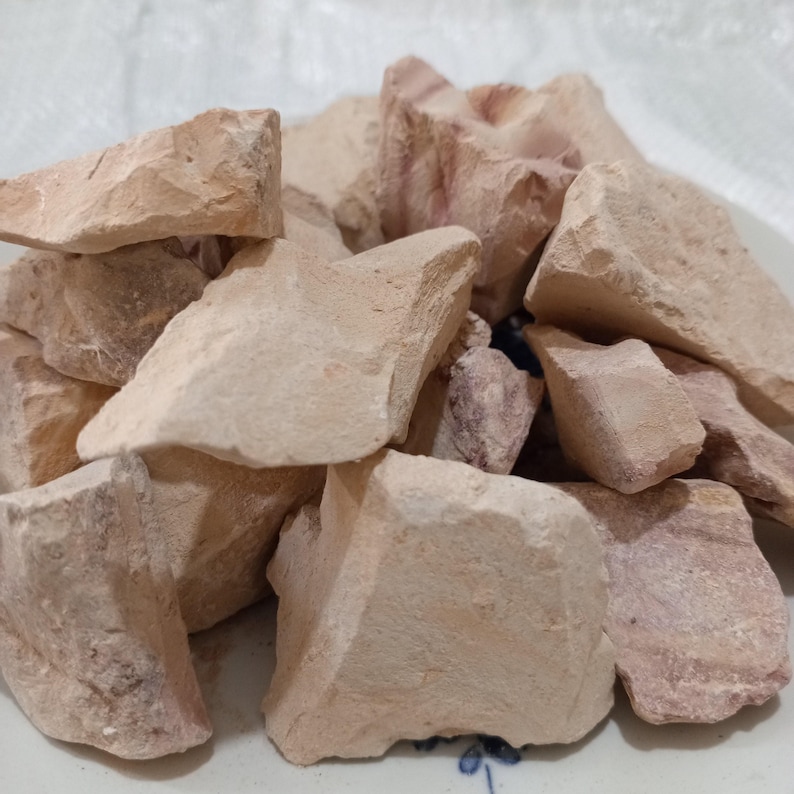 K&ouml;nnte beinhalten: Ein Haufen roher Tonbrocken in verschiedenen Gr&ouml;&szlig;en und Formen. Der Ton hat eine hellbraune Farbe mit rosa und roten Farbt&ouml;nen. Die raue Textur und die unregelm&auml;&szlig;igen Formen deuten auf ein nat&uuml;rliches, unverarbeitetes Material hin, m&ouml;glicherweise f&uuml;r Bastel- oder Kosmetikzwecke.