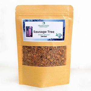 Könnte beinhalten: Ein brauner Papiersack mit einem transparenten Fenster, das eine braune, körnige Substanz zeigt. Ein weißes Etikett mit blauen Akzenten trägt die Aufschrift "Sausage Tree (Kigelia africana) Stem Bark" und ein Bild von rosa Wurstbaumfrüchten.