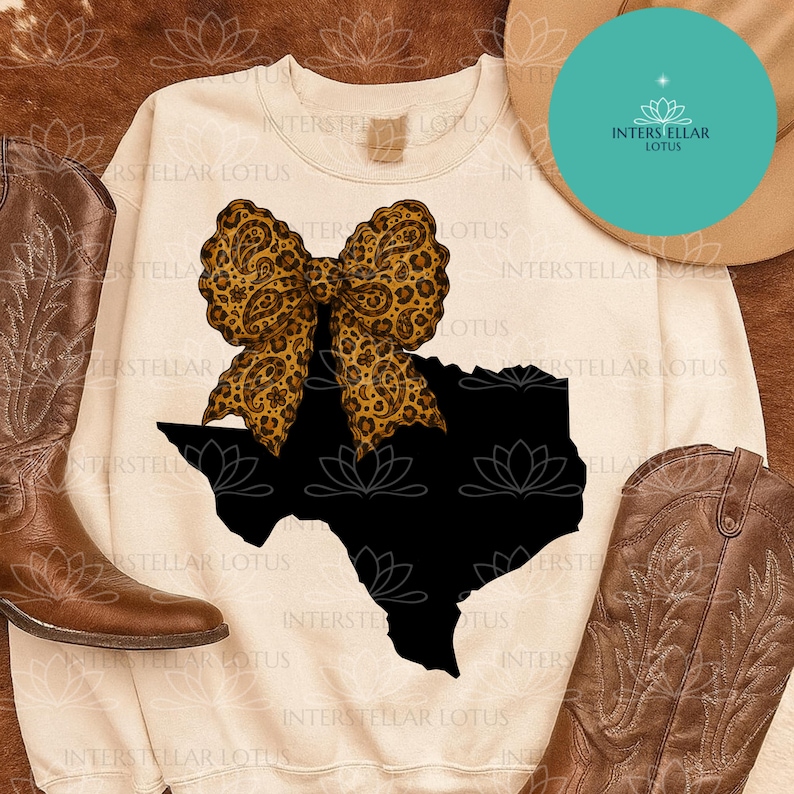 May include: Cream-colored sweatshirt featuring a black Texas outline with a leopard print bow. The design is centered on the front of the shirt. The words "INTERSTELLAR LOTUS" are printed on the shirt. Brown cowboy boots are on either side.
