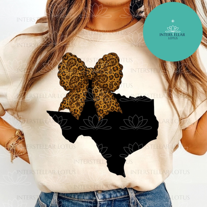 May include: A beige t-shirt featuring a black silhouette of the state of Texas, topped with a large bow. The bow has a leopard print design. The shirt has the text "INTERSTELLAR LOTUS" in a teal circle.