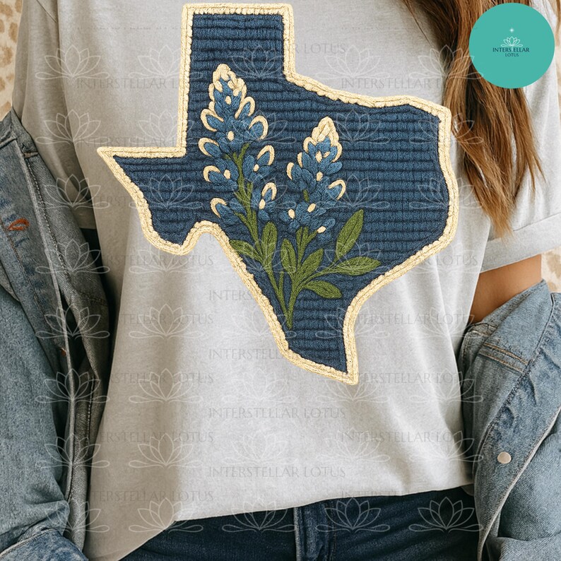 May include: A light gray t-shirt featuring a blue Texas-shaped patch with a bluebonnet flower design. The patch has a textured appearance with a cream-colored border. The shirt is paired with a denim jacket.