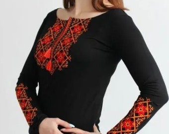 May include: Black long-sleeved shirt with red and orange embroidered details on the chest and sleeves. The embroidery features geometric patterns.