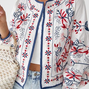 Puede incluir: Una chaqueta blanca bordada con ribete azul y patrones florales en rojo, rosa y azul.
