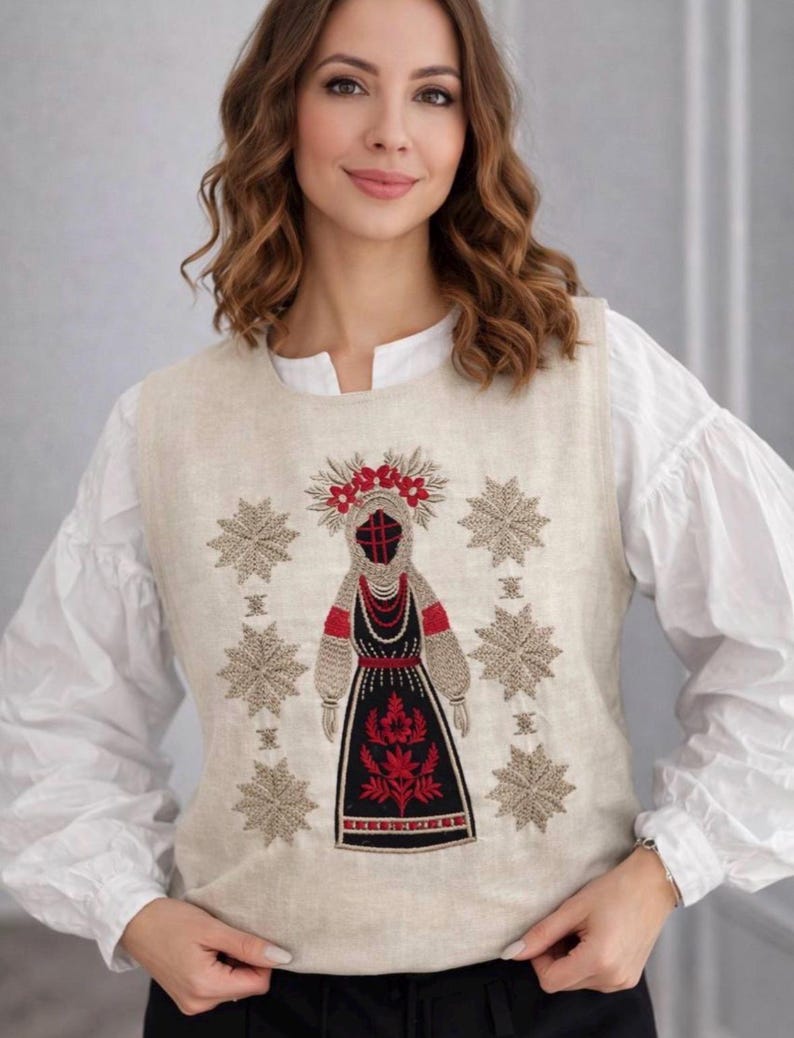 May include: A sleeveless beige linen vest featuring intricate embroidery of a central figure in traditional attire surrounded by six large star-shaped patterns. The embroidery uses black, red, and beige thread to create detailed motifs.