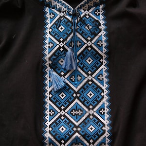 May include: Black shirt with intricate blue and white embroidered geometric patterns. The design features diamond and cross motifs, with a detailed collar and tassel ties. A small illustration is visible at the bottom right.